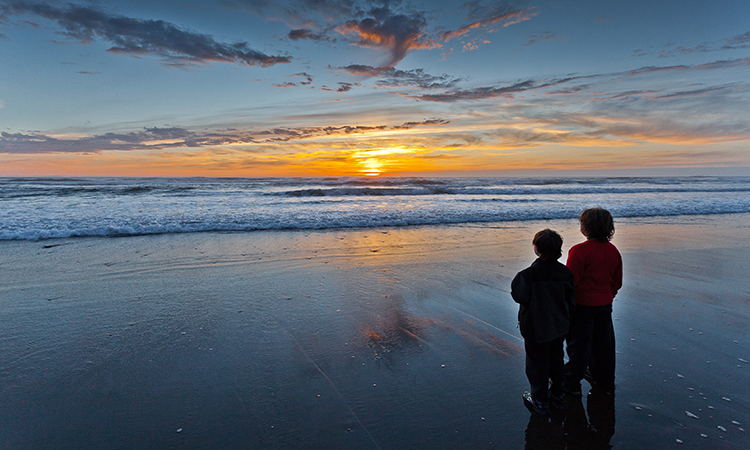 Dos niños mirando al horizonte con una puesta de sol costera. Foto de Quentin Surco.